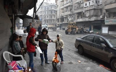 Des enfants syriens rassemblés autour d'un feu dans les rues d'Alep, pendant l'offensive gouvernementale pour reprendre la ville, le 27 décembre 2016. (Crédit : George Ourfalian/AFP)