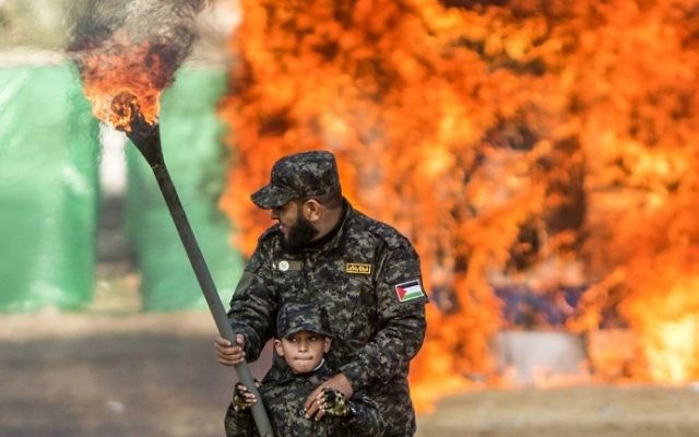 Un Palestinien aide un petit garçon à enflammer un drapeau israélien pendant la cérémonie de fin d'un programme de formation militaire du Hamas, à Gaza Ville, le 22 janvier 2017. (Crédit : Mahmud Hams/AFP)