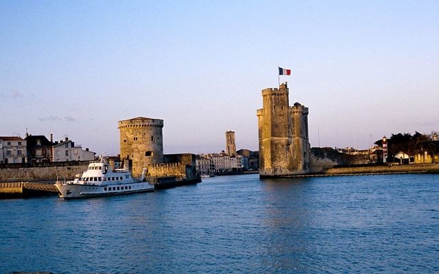 L' avant port de La Rochelle un soir de coucher de soleil doré au mois de mai. A droite, la Tour Saint-Nicolas, à l' arrière plan le clocher de l' église Saint-Sauveur, à gauche, la Tour de la Chaîne. Plus en avant, "L'Ilienne" (1973, IMO 7336185) amarré au ponton d' embarquement des "Croisières Inter-Îles", entreprise de tourisme qui organise des excursions et des promenades en mer vers les îles avoisinantes. La Rochelle, Charente Maritime, France (Crédit : Jpbazard/CC BY SA 3.0) L' avant port de La Rochelle un soir de coucher de soleil doré au mois de mai. A droite, la Tour Saint-Nicolas, à l' arrière plan le clocher de l' église Saint-Sauveur, à gauche, la Tour de la Chaîne. Plus en avant, "L'Ilienne" (1973, IMO 7336185) amarré au ponton d' embarquement des "Croisières Inter-Îles", entreprise de tourisme qui organise des excursions et des promenades en mer vers les îles avoisinantes. La Rochelle, Charente Maritime, France (Crédit : Jpbazard/CC BY SA 3.0)