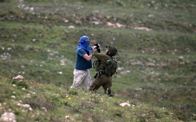 Un soldat israélien lutte contre un Israélien masqué habitant dans une implantation, au sud de Naplouse, en Cisjordanie, le 30 mars 2017. (Crédit : Jaafar Ashtiyeh/AFP) Un soldat israélien lutte contre un Israélien masqué habitant dans une implantation, au sud de Naplouse, en Cisjordanie, le 30 mars 2017. (Crédit : Jaafar Ashtiyeh/AFP)