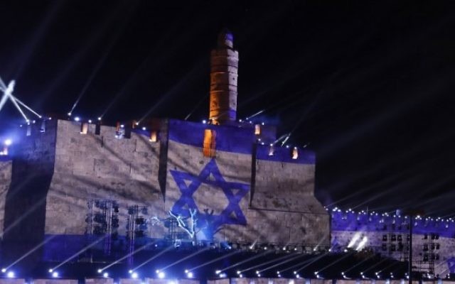 Les gens regardent une projection du drapeau israélien au cours d'un spectacle de son et lumière projeté sur les murs de la Vieille ville de Jérusalem pour célébrer le début de la semaine du 50ème anniversaire de la guerre israélo-arabe de 1967, le 20 mai 2017 (Crédit : GALI TIBBON / AFP PHOTO)