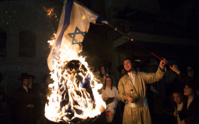 Un membre de la secte anti-sioniste Neturei Karta brûle un drapeau israélien pendant la fête de Lag BaOmer, dans le quartier ultra-orthodoxe de Mea Shearim, à Jérusalem, en mai 2014. (Crédit : Yonatan Sindel/Flash90)