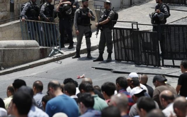 Les forces de sécurité israéliennes surveillent les fidèles musulmans palestiniens qui prient à l'extérieur de la Porte des Lions, une entrée principale du mont de Tempe dans la Vieille Ville de Jérusalem, le 22 juillet 2017. (Crédit : AFP / Ahmad Gharabli)