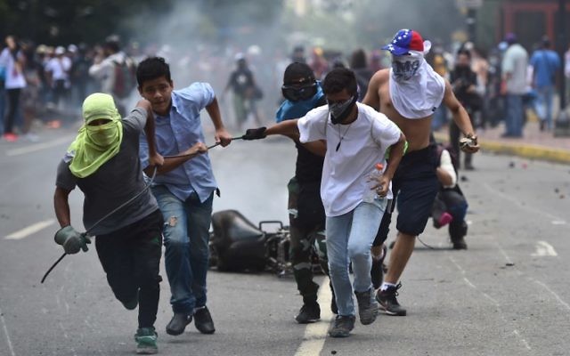 Les militants anti-gouvernementistes font glisser une moto de police brûlée après l'explosion d'un engin explosif lors d'une manifestation contre les élections d'une assemblée constituante à Caracas le 30 juillet 2017. (Crédit : AFP / Ronaldo SCHEMIDT)