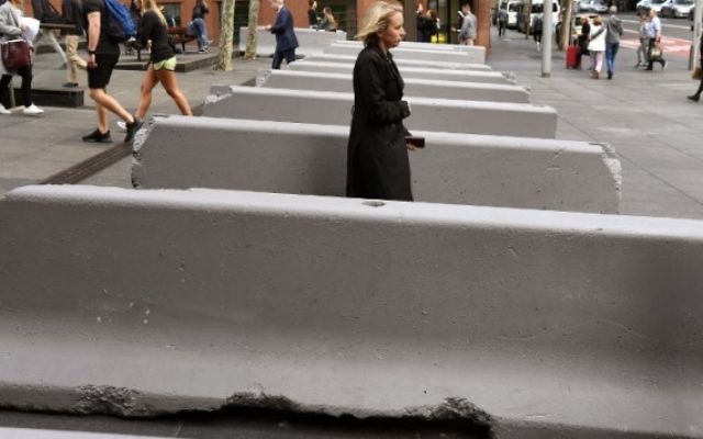 Les piétons passent à côté des bornes de sécurité en béton installées près du Lindt Cafe, où un homme a pris en otage des clients en 2014,  le 17 juillet 2017 (Crédit : AFP / WILLIAM WEST)