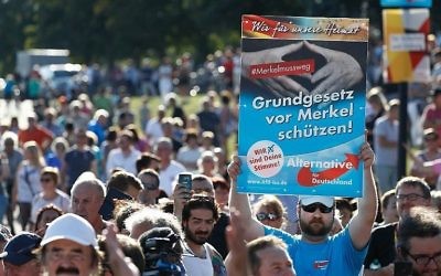 Un partisan du parti nationaliste de l'AfD brandit une pancarte disant "Protégeons la constitution de [l'attaque de] Merkel" alors que la chancelière allemande s'exprime lors d'un rassemblement de campagne électorale de son parti chrétien du CDU à Bitterfeld, en Allemagne, le 29 août 2017. (Crédit : Odd Andersen/AFP)