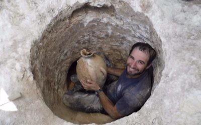 David Tanami, archéologue de l'Autorité israélienne des Antiquités, s'active autour de l'ouverture étroite d'une tombe pour en sortir une jarre sur un site funéraire cananéen aux abords du zoo biblique de Jérusalem (Crédit : Shua Kisilevitz, Autorité israélienne des antiquités)