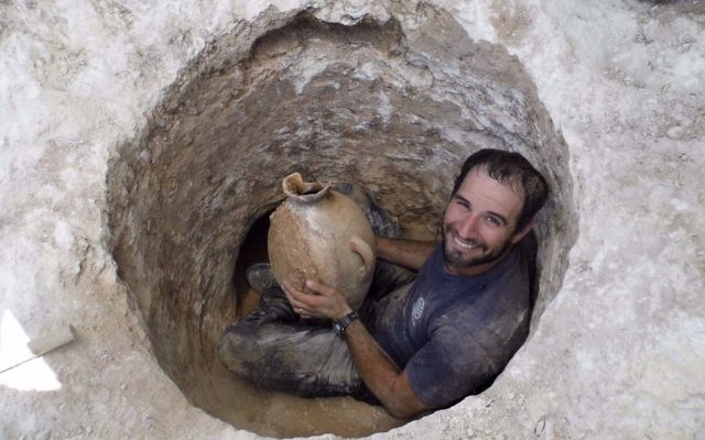 David Tanami, archéologue de l'Autorité israélienne des Antiquités, s'active autour de l'ouverture étroite d'une tombe pour en sortir une jarre sur un site funéraire cananéen aux abords du zoo biblique de Jérusalem (Crédit : Shua Kisilevitz, Autorité israélienne des antiquités)