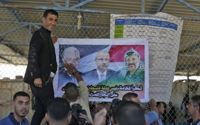 Des Palestiniens mettent un poster à l'effigie du leader palestinien Mahmoud Abbas, à gauche, du Premier ministre  Rami Hamdallah et de feu  Yasser Arafat à l'entrée  nord de la bande de Gaza, juste après le poste-frontière d'Erez contrôlé par les Israéliens, le 1er novembre 2017 à  Beit Hanoun. (Crédit : MAHMUD HAMS / AFP)