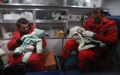 Des ambulanciers syriens distraient des enfants dans une ambulance, pendant la deuxième nuit de l’opération d’évacuation coordonnée par le Croissant rouge syrien et le CICR, à Douma, dans la région de la Ghouta orientale, le 27 décembre 2017. (Crédit : AFP/ABDULMONAM EASSA)