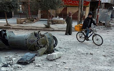 Des hommes passent devant les restes d'une roquette dans la ville de Douma, dans la région assiégée de la Ghouta aux abords de la capitale de Damas, suite aux frappes aériennes menées par les forces du régime, le 23 février 2018 (Crédit :  AFP PHOTO / HAMZA AL-AJWEH)