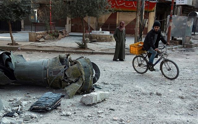Des hommes passent devant les restes d'une roquette dans la ville de Douma, dans la région assiégée de la Ghouta aux abords de la capitale de Damas, suite aux frappes aériennes menées par les forces du régime, le 23 février 2018 (Crédit : AFP PHOTO / HAMZA AL-AJWEH) Des hommes passent devant les restes d'une roquette dans la ville de Douma, dans la région assiégée de la Ghouta aux abords de la capitale de Damas, suite aux frappes aériennes menées par les forces du régime, le 23 février 2018 (Crédit : AFP PHOTO / HAMZA AL-AJWEH)