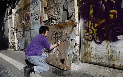L'artiste de rue née en Israël et qui vit à New York Sara Erenthal dessine l'un de ses visages emblématiques de femme dans la ville côtière israélienne de Tel Aviv, le 28 janvier 2018 (Crédit :   AFP PHOTO / MENAHEM KAHANA)