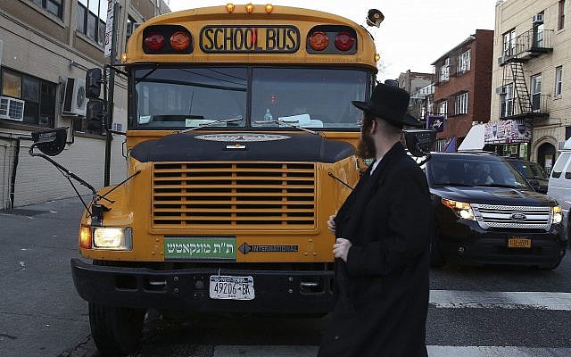 Illustration : Un juif ultra-orthodoxe marche devant un autobus scolaire juif, qui a un signe yiddish sur le devant, dans le quartier de Borough Park à Brooklyn, le 1er janvier 2014 (Crédit : Nati Shohat / Flash90)