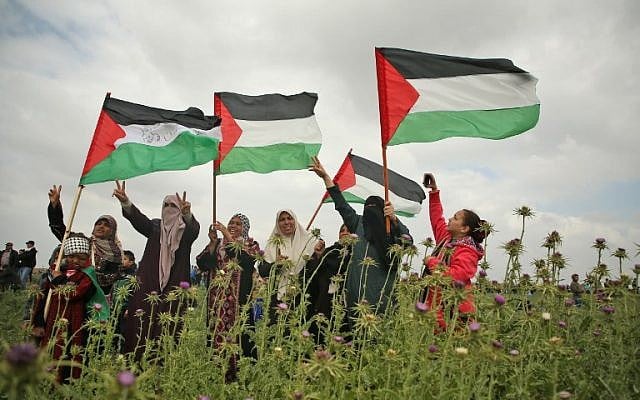 Des femmes palestiniennes brandissent des drapeaux et font le signe de la victoire durant une manifestation aux abords de la frontière avec Israël, à l'est de Jabalia, dans la bande de Gaza, le 30 mars 2018 (Crédit : AFP PHOTO / Mohammed ABED)