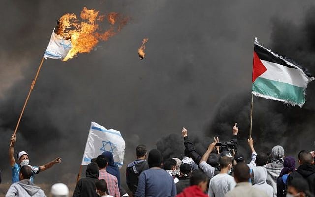 Des manifestants palestiniens brûlent des drapeaux israéliens près de la barrière frontalière avec Israël, à l'est de Khan Yunis dans le sud de la ville de Gaza, le 13 avril 2018 (Crédit : AFP / Thomas Coex)