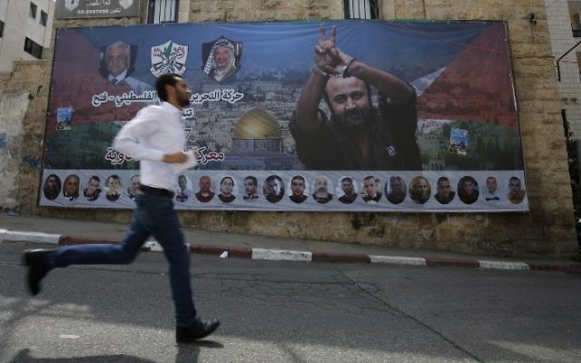 Un Palestinien passe devant une affiche avec le portrait du terroriste condamné et célèbre prisonnier palestinien Marwan Barghouti dans la ville de Ramallah, en Cisjordanie, le 3 mai 2017. (AFP/ ABBAS MOMANI) Un Palestinien passe devant une affiche avec le portrait du terroriste condamné et célèbre prisonnier palestinien Marwan Barghouti dans la ville de Ramallah, en Cisjordanie, le 3 mai 2017. (AFP/ ABBAS MOMANI)