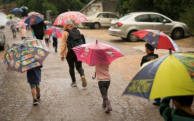 Des enfants s'abritent sous des parapluies au Kibbutz Sarid, dans le nord d'Israël, le 25 avril 2018. (Crédit : Anat Hermony/Flash90)