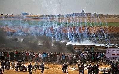 Des émeutiers palestiniens au milieu des gaz lacrymogènes et de la fumée émanant des pneus brûlés, à l'est de Gaza City, le 14 mai 2018. (Crédit : AFP/ Mohammed Abed) Des émeutiers palestiniens au milieu des gaz lacrymogènes et de la fumée émanant des pneus brûlés, à l'est de Gaza City, le 14 mai 2018. (Crédit : AFP/ Mohammed Abed)