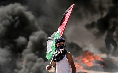 Un jeune garçon brandit un drapeau palestinien pendant les émeutes à la frontière avec Gaza, le 14 mai 2018. (Crédit :
MAHMUD HAMS / AFP)
