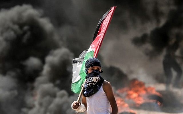 Un jeune garçon brandit un drapeau palestinien pendant les émeutes à la frontière avec Gaza, le 14 mai 2018. (Crédit :
MAHMUD HAMS / AFP)