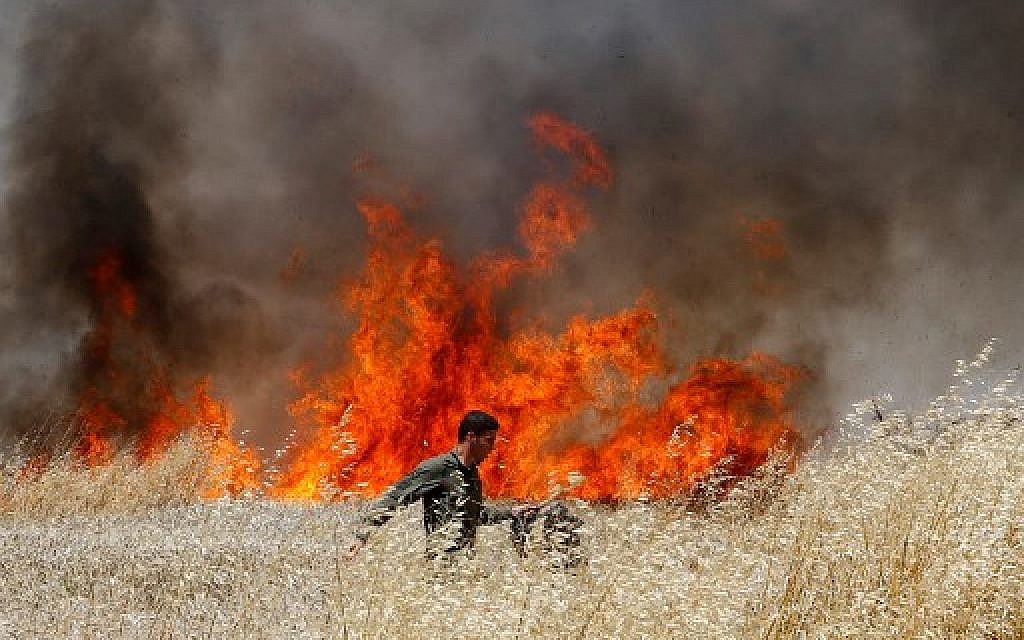 Un soldat israélien tente d'éteindre un feu dans un champ de blé du kibboutz Nahal Oz, incendié par des cerfs-volants envoyés depuis Gaza par des émeutiers, le 14 mai 2018. (Crédit : AFP / JACK GUEZ)