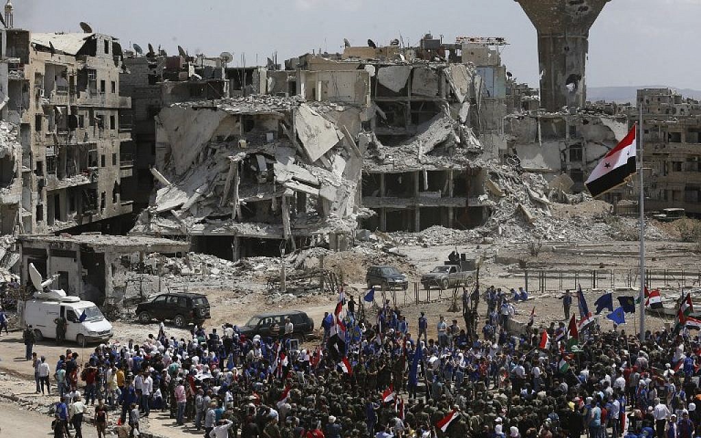 Des manifestants pro-régimes dressent un drapeau à l'entrée du quartier de Hajar al-Aswad, en périphérie de Damas, le 24 mai 2018. (Crédit : AFP/Louai Beshara) Des manifestants pro-régimes dressent un drapeau à l'entrée du quartier de Hajar al-Aswad, en périphérie de Damas, le 24 mai 2018. (Crédit : AFP/Louai Beshara)