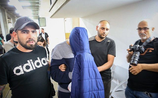 Un homme soupçonné d'avoir tué ses deux soeurs dans leur maison de Jaffa se couvre le visage à son arrivée à la cour des magistrats de Tel Aviv pour une audience de mise en détention, le 17 mai 2018 (Crédit :  FLASH90)