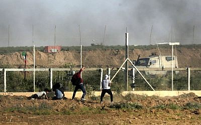 Un Palestinien jette des pierres sur les forces israéliennes alors que de la fumée s'élève des pneus brûlés durant une manifestation le long de la frontière avec la bande de Gaza, à l'est de Gaza city, le 1er juin 2018 (Crédit :  / AFP PHOTO / Mahmud Hams)