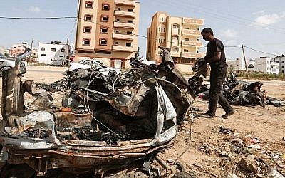 Un Palestinien inspecte une voiture détruite après une frappe israélienne à Gaza City qui, selon l'armée, a été prise pour cible parce qu'elle appartenait à un responsable des attaques aux cerfs-volants et aux ballons incendiaires sur le sud d'Israël, le 17 juin 2018 (Crédit : Mahmud Hams/AFP)