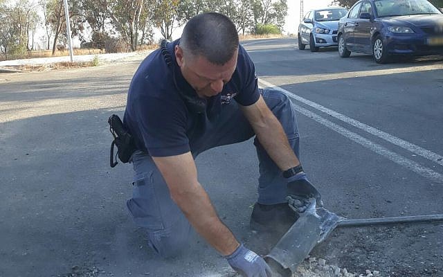 Un pompier tient entre les mains  une roquette tirée depuis Gaza qui est tombée dans la rue de l'une des communautés de la région d'Eshkol, le 20 juin 2018 (Crédit : Police israélienne)