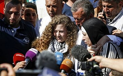 La militante palestinienne Ahed Tamimi, au centre, parle aux journalistes à sa sortie de prison après une pine de huit mois pour avoir giflé des soldats israéliens, accompagnée de son père (au centre-droit) et de sa mère (à droite), à Nabi Saleh, en Cisjordanie, le 29 juillet 2018 (Crédit :  / AFP PHOTO / ABBAS MOMANI)