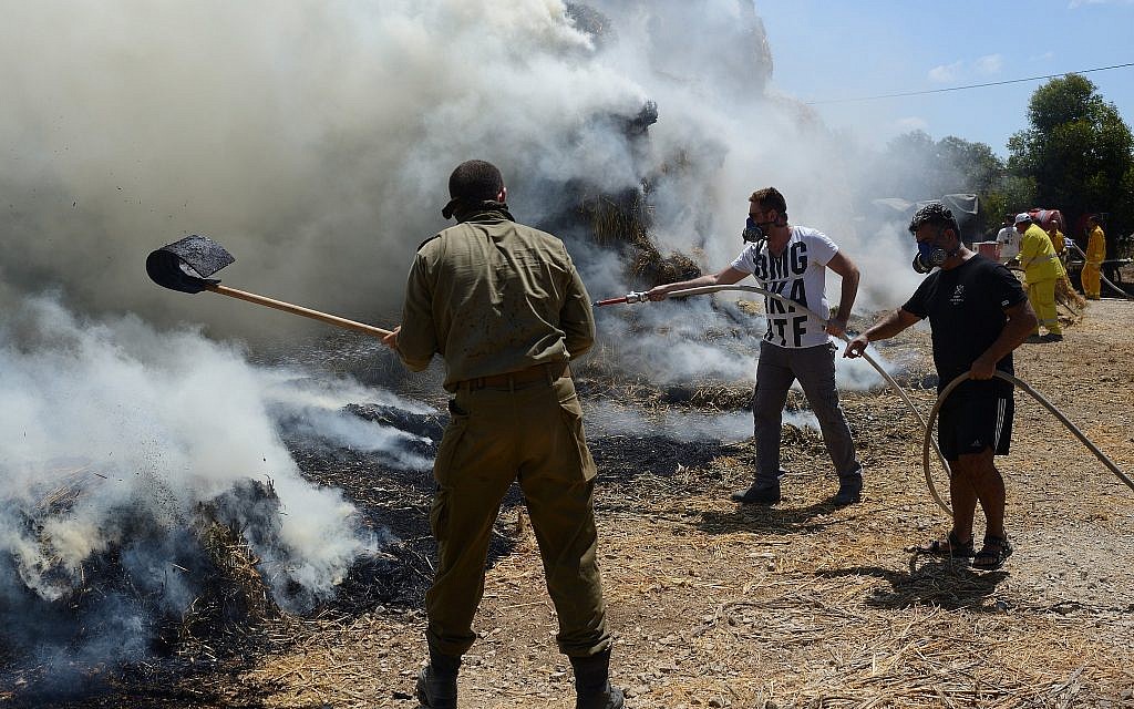 Les pompiers israéliens et les équipes de sécurité luttent contre un incendie près d'un élevage de bovins, allumé par un dispositif incendiaire lancé depuis la bande de Gaza au  Kibbutz Nahal-Oz, le 21 juillet 2018 (Crédit :  Gili Yaari/FLASH90)