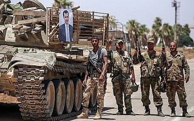 Des soldats du régime syrien à côté d'une photo du président syrien Bashar el-Assad sur un tank, au poste-frontière de Nassib avec la Jordanie, dans la province de Deraa, au sud, le 7 juillet 2018 (Crédit : AFP Photo/Youssef Karwashan)