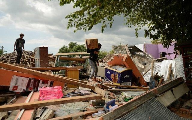 Un jeune homme récupère ses effets personnels alors qu'il grimpe sur les débris d'une maison effondrée à Kayangan, au nord de l'île de Lombok, le 9 août 2018, à la suite du séisme du 5 août. (Crédit : SONNY TUMBELAKA / AFP) Un jeune homme récupère ses effets personnels alors qu'il grimpe sur les débris d'une maison effondrée à Kayangan, au nord de l'île de Lombok, le 9 août 2018, à la suite du séisme du 5 août. (Crédit : SONNY TUMBELAKA / AFP)