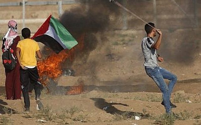 Un manifestant palestinien utilise un lance-pierre alors que d'autres se tiennent près d'un pneu en flammes et agitent un drapeau national lors d'une manifestation le long de la clôture de la frontière à l'est de Gaza le 14 septembre 2018. (AFP PHOTO / Said KHATIB) Un manifestant palestinien utilise un lance-pierre alors que d'autres se tiennent près d'un pneu en flammes et agitent un drapeau national lors d'une manifestation le long de la clôture de la frontière à l'est de Gaza le 14 septembre 2018. (AFP PHOTO / Said KHATIB)
