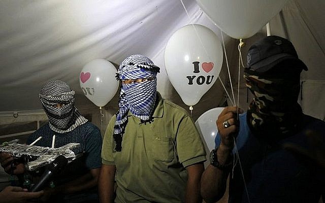 Des Palestiniens cagoulés qui se font appelé 'l'unité de la confusion de la nuit" tiennent des dispositifs incendiaires attachés à des ballons qui vont être lancés en Israël, depuis Rafah, le 26 septembre 2018. (Crédit : AFP /Said Khatib)