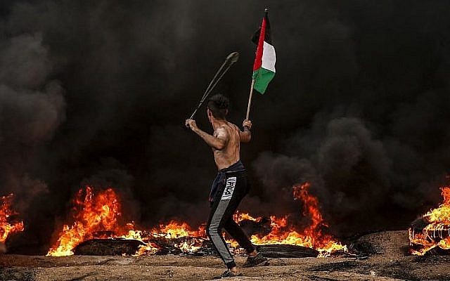Un Palestinien tient un drapeau palestinien alors qu'il utilise une fronde pour lancer des pierres sur les troupes israéliennes lors d'affrontements près de la frontière avec Israël, à l'est de Gaza City, le 26 octobre 2018. (Crédit : Mahmud Hams / AFP) Un Palestinien tient un drapeau palestinien alors qu'il utilise une fronde pour lancer des pierres sur les troupes israéliennes lors d'affrontements près de la frontière avec Israël, à l'est de Gaza City, le 26 octobre 2018. (Crédit : Mahmud Hams / AFP)