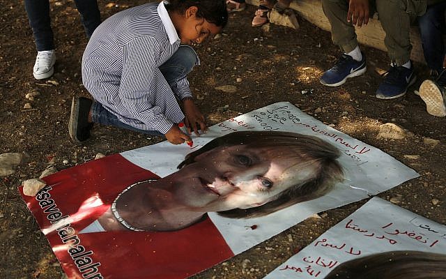 Une enfant bédouine écrit sur une photo de la chancelière allemande Angela Merkel avant sa visite prévue en Israël le mercredi 2 octobre 2018, dans la communauté bédouine de Khan al-Ahmar, en Cisjordanie. Des enfants supplient Merkel de faire pression sur Israël pour qu'il mette fin aux plans de démolition d'un campement de baraques en carton ondulé aux abords d'une implantation israélienne située à l'Est de Jérusalem. On peut lire en arabe sur l'affiche : "Sauvez Khan al-Ahmar" et "Sauvez notre école". (AP Photo/Nasser Shiyoukhi)