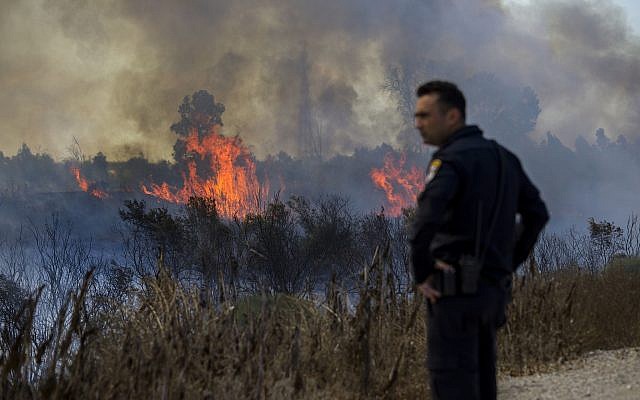 Un policier israélien regarde un incendie déclenché par un ballon transportant un tissu en feu, lancé par des Palestiniens de la bande de Gaza dans la réserve naturelle de Karmia, le jeudi 11 octobre 2018 (Crédit : AP/Tsafrir Abayov) Un policier israélien regarde un incendie déclenché par un ballon transportant un tissu en feu, lancé par des Palestiniens de la bande de Gaza dans la réserve naturelle de Karmia, le jeudi 11 octobre 2018 (Crédit : AP/Tsafrir Abayov)