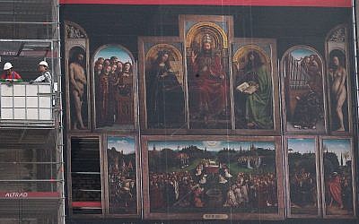 Des ouvriers dans une nacelle à côté de la reproduction géante de l'oeuvre de 'l'Adoration de l'Agneau mystique' du peintre flamand Jan van Eyck pendant la rénovation de la cathédrale Saint-Bavo de Gand, en Belgique, le 13 mars 2014 (Crédit : AP Photo/Yves Logghe)