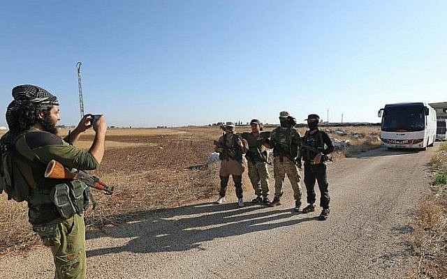 Les membres du groupe Hayat Tahrir al-Sham, dirigé par lancien affilié d'Al-Qaïda en Syrie, devant un convoi de bus prêts à entrer à  Fuaa et à Kefraya pour évacuer les habitants, le 18 juillet 2018 (Crédit : AFP PHOTO / OMAR HAJ KADOUR)
