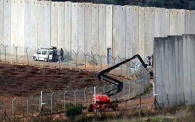 Des Israéliens travaillent près du mur frontalier en béton séparant les deux pays,  une photo prise au sud du village libanais de Kfar Kila, à la frontière avec Israël, le 9 décembre 2018 (Crédit :  Ali DIA / AFP)