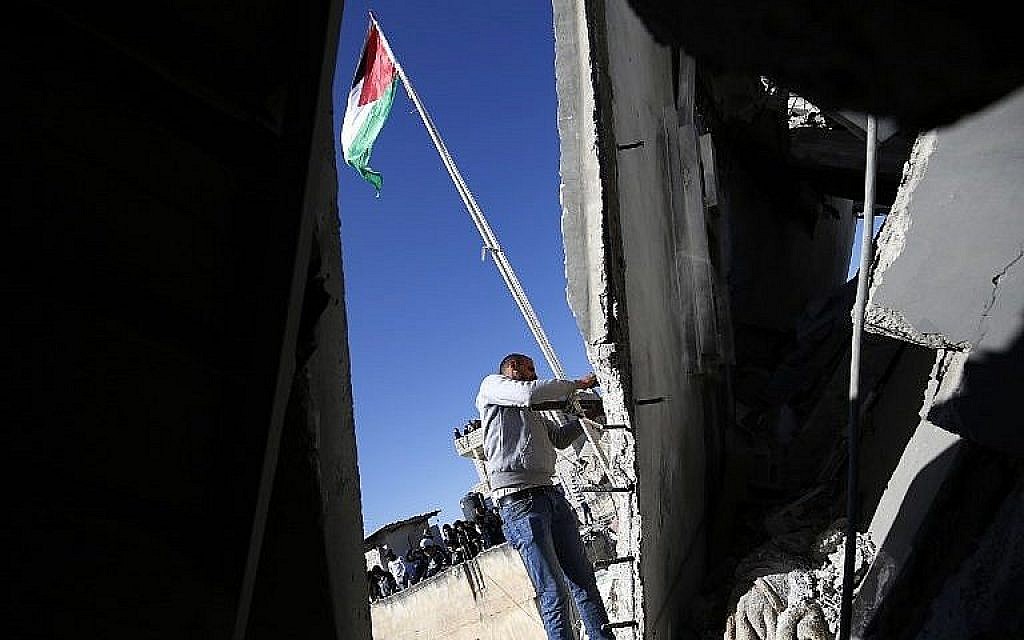 Un homme hisse le drapeau palestinien sur les ruines d'une mansion appartenant à un Palestinien accusé d'avoir tué un soldat israélien dans le camp de réfugiés d'Al-Amari en Cisjordanie, après sa destruction par l'armée israélienne, le 15 décembre 2018 (Crédit :  Abbas Momani/AFP)