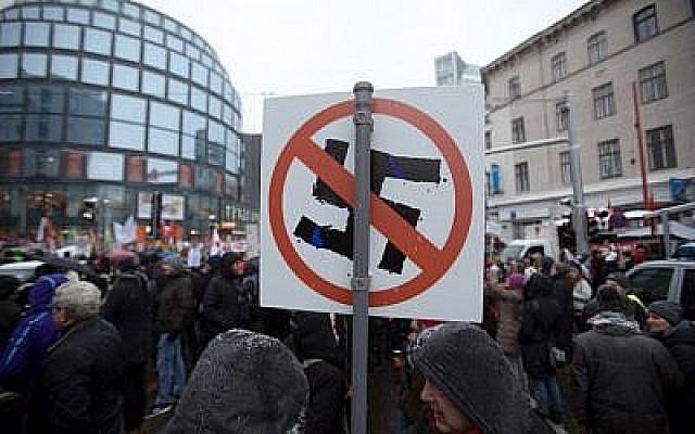 Les manifestants brandissent une pancarte avec une croix gammée barrée lors d'un rassemblement organisé au premier anniversaire de la coalition gouvernementale formée entre les conservateurs et le parti de la Liberté d'extrême droite, le 15 décembre 2018 (Crédit :  ALEX HALADA / AFP)