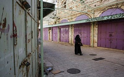 Une Palestinienne marche devant les boutiques fermées pour cause de grève contre le système de sécurité sociale proposé par l'AP, à Hébron, le 15 janvier 2019. (Crédit : HAZEM BADER / AFP) Une Palestinienne marche devant les boutiques fermées pour cause de grève contre le système de sécurité sociale proposé par l'AP, à Hébron, le 15 janvier 2019. (Crédit : HAZEM BADER / AFP)