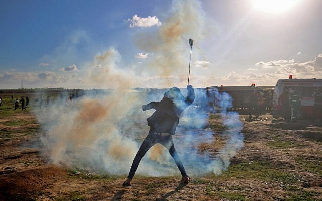 Un émeutier palestinien se sert d'une fronde devant les gaz lacrymogènes lancés par l'armée israélienne lors d'une émeute le long de la frontière en Gaza et Israël, le 18 janvier 2019. (Crédit : SAID KHATIB / AFP) Un émeutier palestinien se sert d'une fronde devant les gaz lacrymogènes lancés par l'armée israélienne lors d'une émeute le long de la frontière en Gaza et Israël, le 18 janvier 2019. (Crédit : SAID KHATIB / AFP)