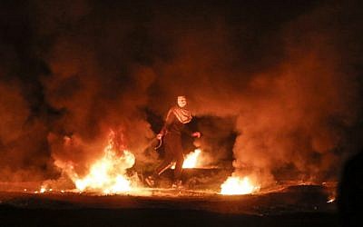 Un manifestant palestinien masqué traîne un pneu en flammes pendant une manifestation nocturne près de la clôture le long de la frontière avec Israël, à l'est de la ville de Gaza, le 11 février 2019. (Photo par MAHMUD HAMS / AFP)