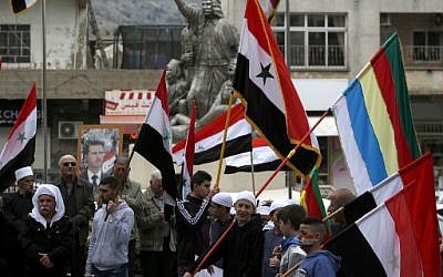 Des habitants du Golan agitent des drapeaux syrien et druze face au portrait du président syrien Bachar al-Assad lors d'une manifestation contre la déclaration du président américain Donald Trump, qui a reconnu sur Twitter le Golan comme appartenant à Israël, dans le village de Majdal Shams, le 23 mars 2019. (Crédit photo : Jalaa MAREY / AFP)
