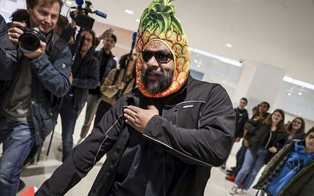 Dieudonné M'bala M'bala, portant un masque représentant un ananas en référence à son expression négationniste 'shoahananas', fait le geste controversé de la "quenelle" à son arrivée au palais de justice de Paris le 26 mars 2019, devant un public amusé. (Crédit : KENZO TRIBOUILLARD / AFP)